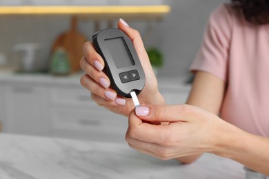 Photo of Diabetes. Woman checking blood sugar level with glucometer at marble table in kitchen, closeup. Space for text