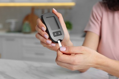 Diabetes. Woman checking blood sugar level with glucometer at marble table in kitchen, closeup. Space for text