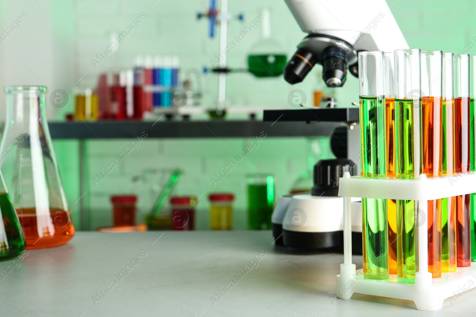 Photo of Different glassware with samples and microscope on table in chemistry laboratory. Space for text