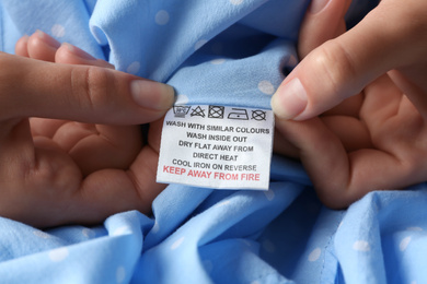 Photo of Woman reading clothing label with care instructions on light blue polka dot garment, closeup