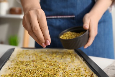 Making delicious baklava. Woman adding chopped nuts to dough at white table, closeup