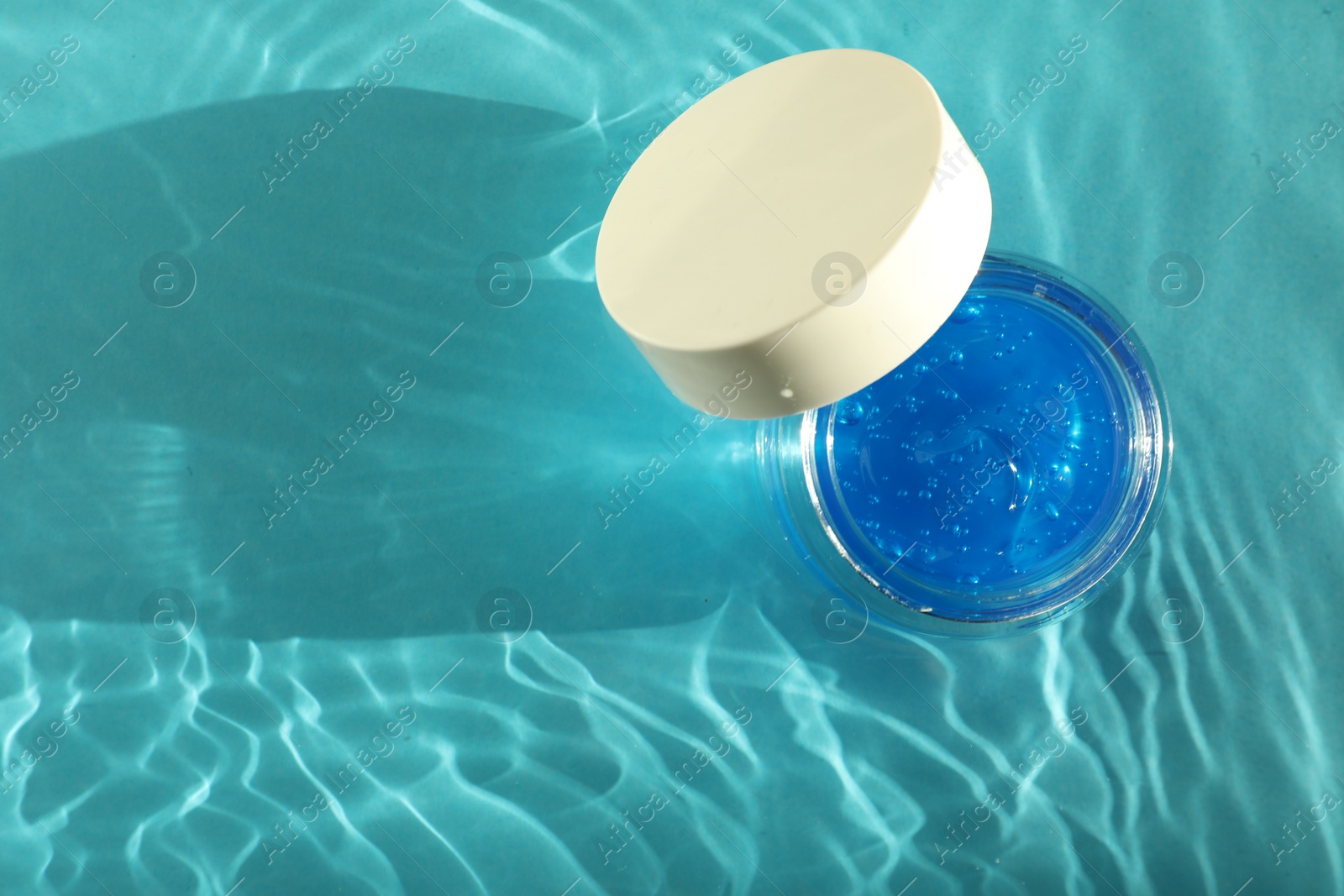 Photo of Open jar of cosmetic product in water on turquoise background, top view. Space for text