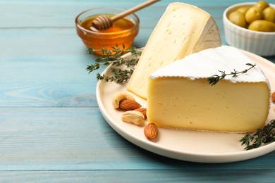 Photo of Tasty Camembert cheese with thyme and nuts on light blue wooden table, space for text