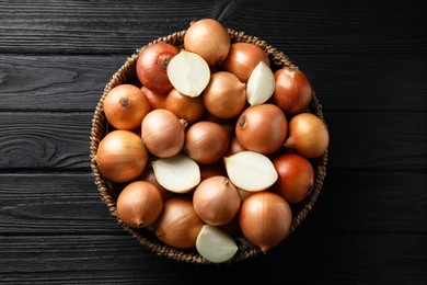 Whole and cut onions on black wooden table, top view