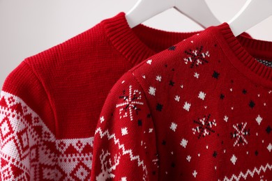 Photo of Christmas sweaters hanging on rack against light background, closeup