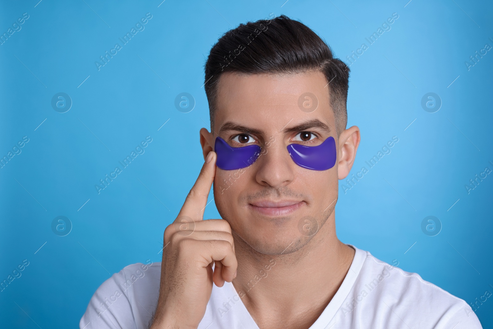 Photo of Man applying under eye patch on light blue background