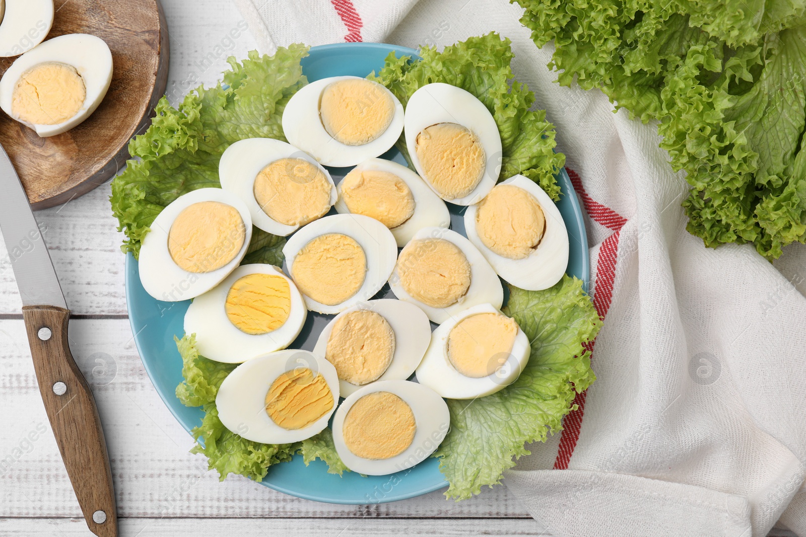 Photo of Fresh hard boiled eggs and lettuce on white wooden table, flat lay