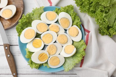 Fresh hard boiled eggs and lettuce on white wooden table, flat lay