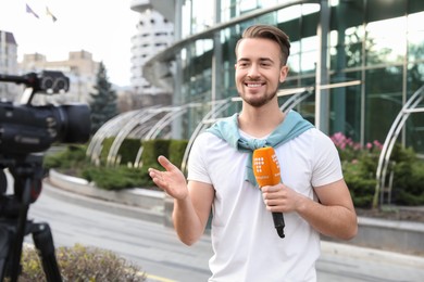 Young male journalist with microphone working on city street