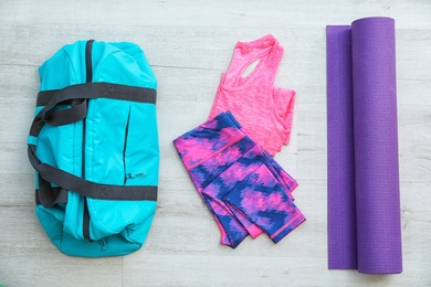 Photo of Flat lay composition with sports bag, sportswear and mat on wooden floor