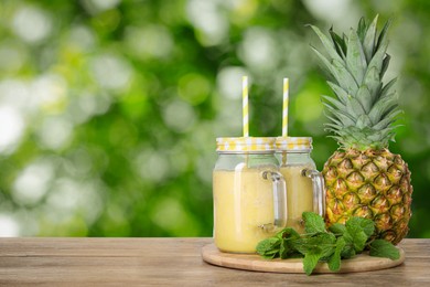 Image of Tasty pineapple smoothie in mason jars on wooden table against blurred background, space for text