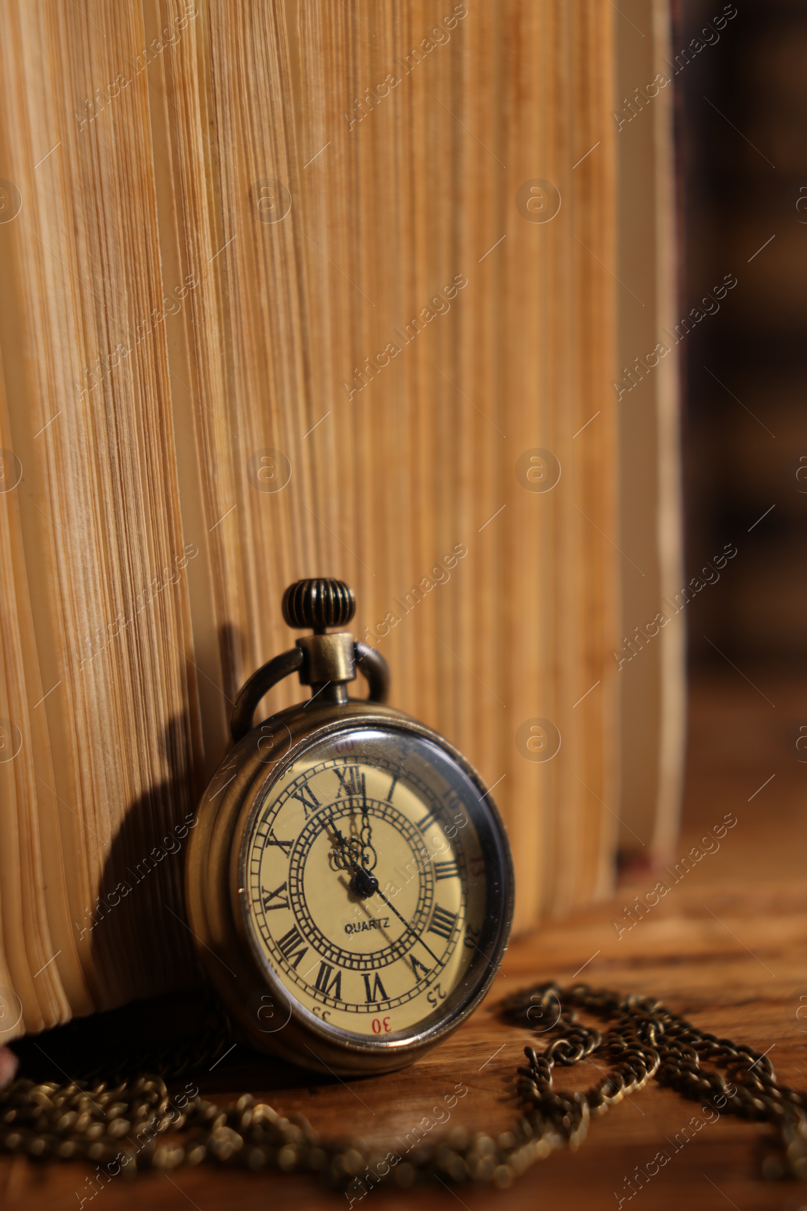 Photo of Pocket clock with chain and book on table, closeup