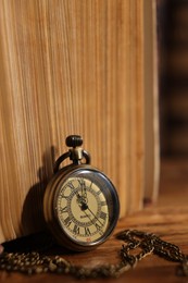 Photo of Pocket clock with chain and book on table, closeup