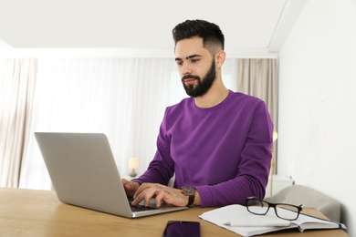 Photo of Handsome young man working with laptop at table in home office