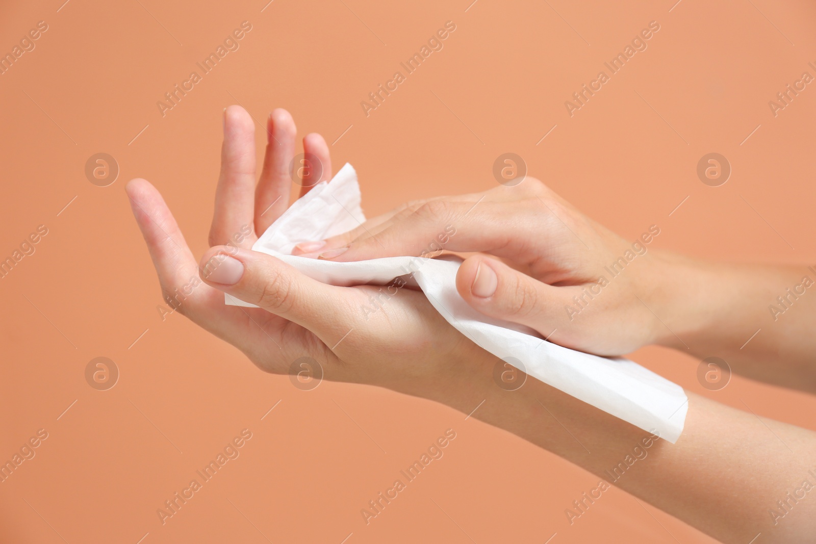 Photo of Woman cleaning hands with paper tissue on light brown background, closeup