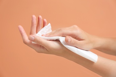 Woman cleaning hands with paper tissue on light brown background, closeup