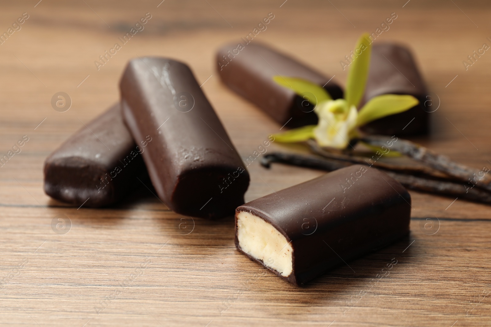 Photo of Glazed curd cheese bars, vanilla pods and flower on wooden table, closeup