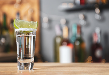 Photo of Mexican Tequila with salt and lime slice on bar counter. Space for text