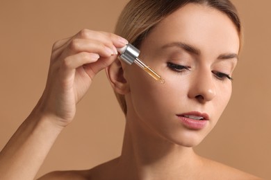 Photo of Beautiful woman applying cosmetic serum onto her face on beige background, closeup