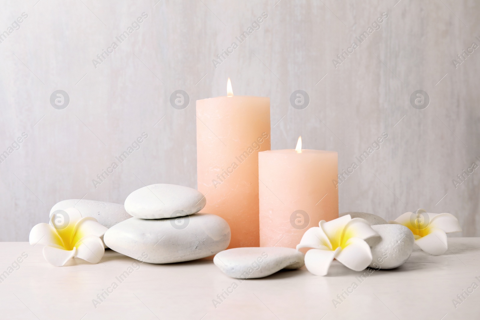 Photo of Zen stones, lighted candles and exotic flowers on table against light background