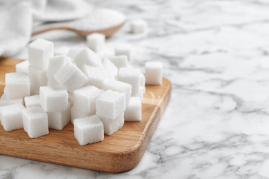 Photo of Refined sugar cubes on white marble table. Space for text