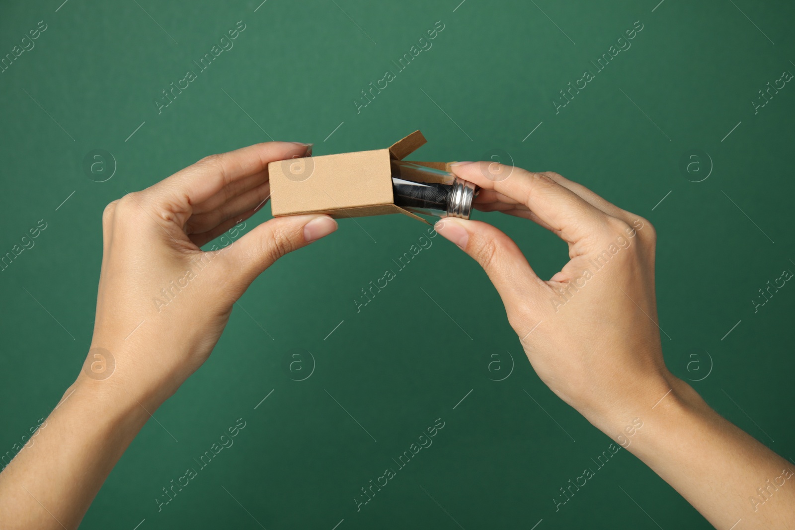Photo of Woman holding cardboard package and glass jar with biodegradable dental floss against green background, closeup