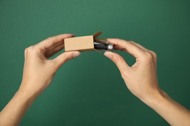 Photo of Woman holding cardboard package and glass jar with biodegradable dental floss against green background, closeup