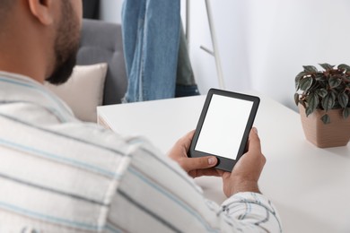 Photo of Man using e-book reader at white table indoors, closeup