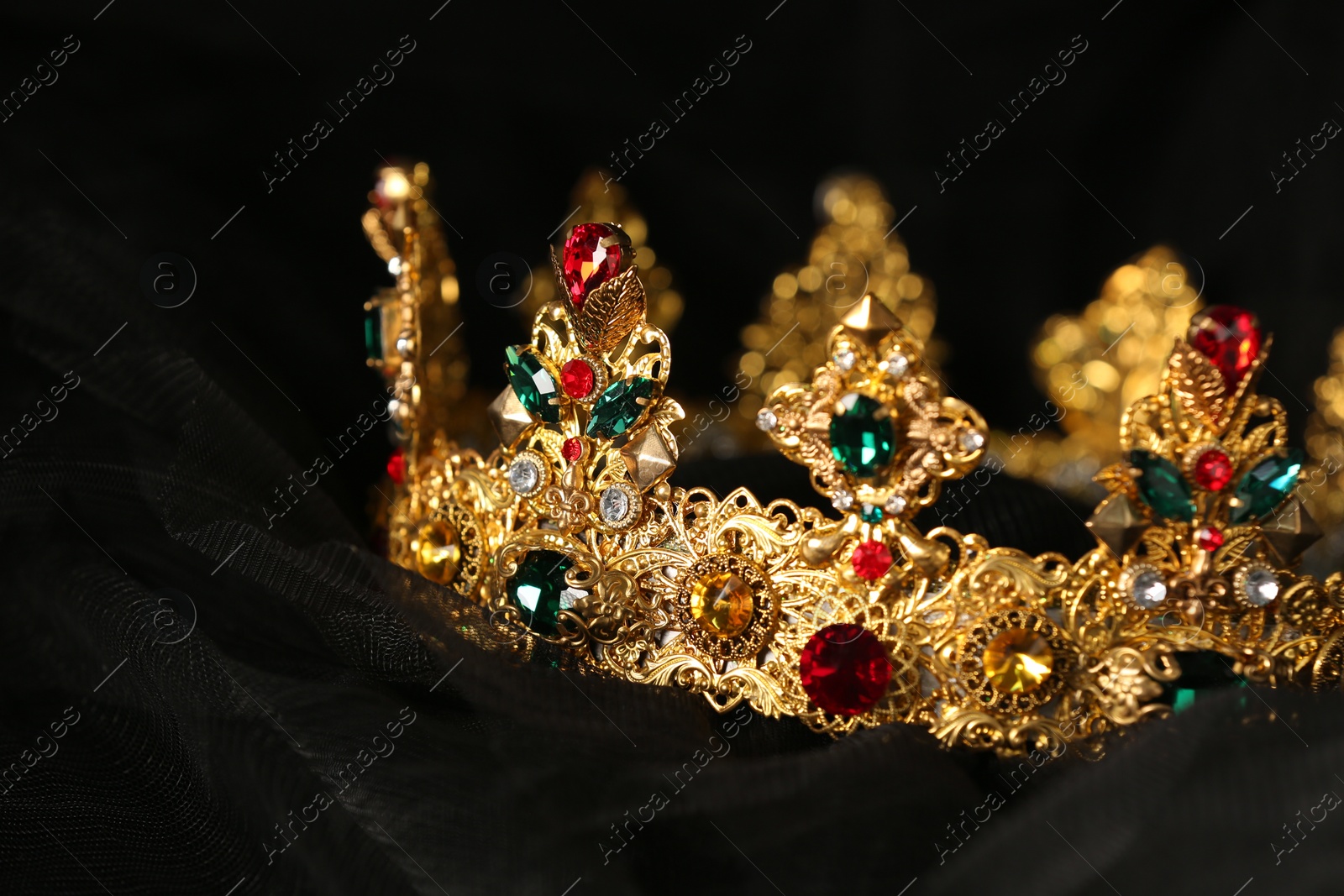 Photo of Beautiful golden crown with gems on black cloth, closeup