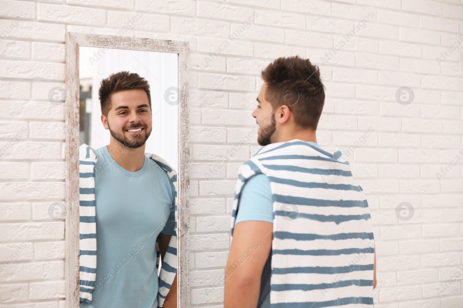 Photo of Young man looking at himself in large mirror at home