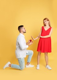 Photo of Young woman rejecting engagement ring from boyfriend on yellow background