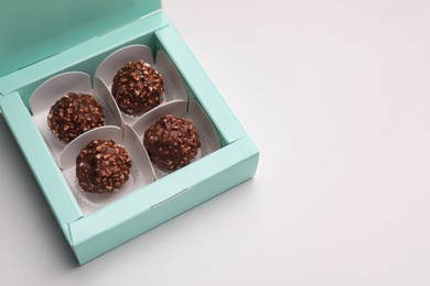 Photo of Delicious chocolate candies in turquoise box on light grey background, space for text. Production line