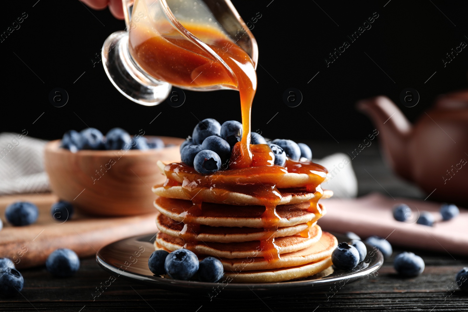 Photo of Pouring caramel syrup onto pancakes with fresh blueberries on table