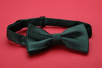 Photo of Stylish black bow tie with polka dot pattern on red background