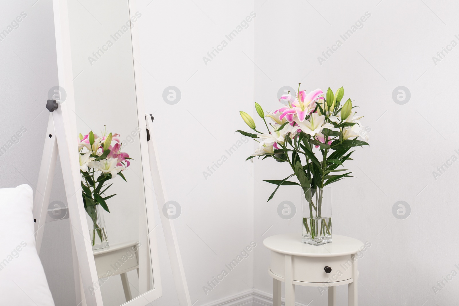 Photo of Vase with bouquet of beautiful lilies on white table near mirror