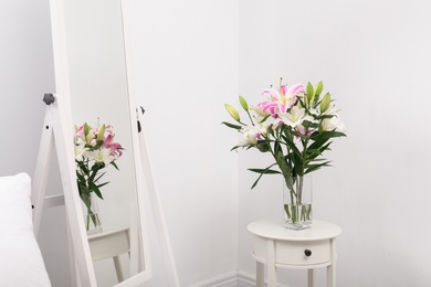 Photo of Vase with bouquet of beautiful lilies on white table near mirror