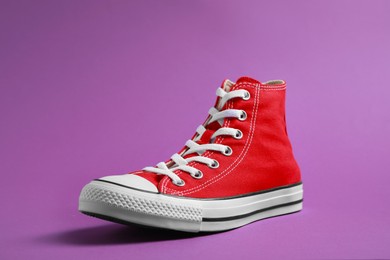 Photo of One new stylish red sneaker on purple background