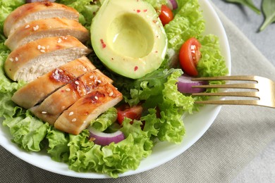 Eating delicious salad with chicken, avocado and vegetables at table, top view