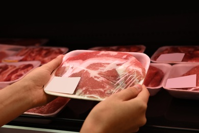 Woman taking packed pork meat from shelf in supermarket