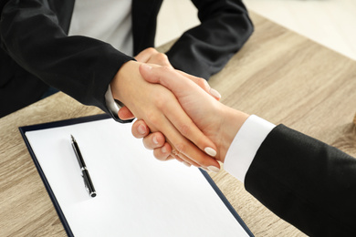 Real estate agent shaking hands with client at table in office, closeup