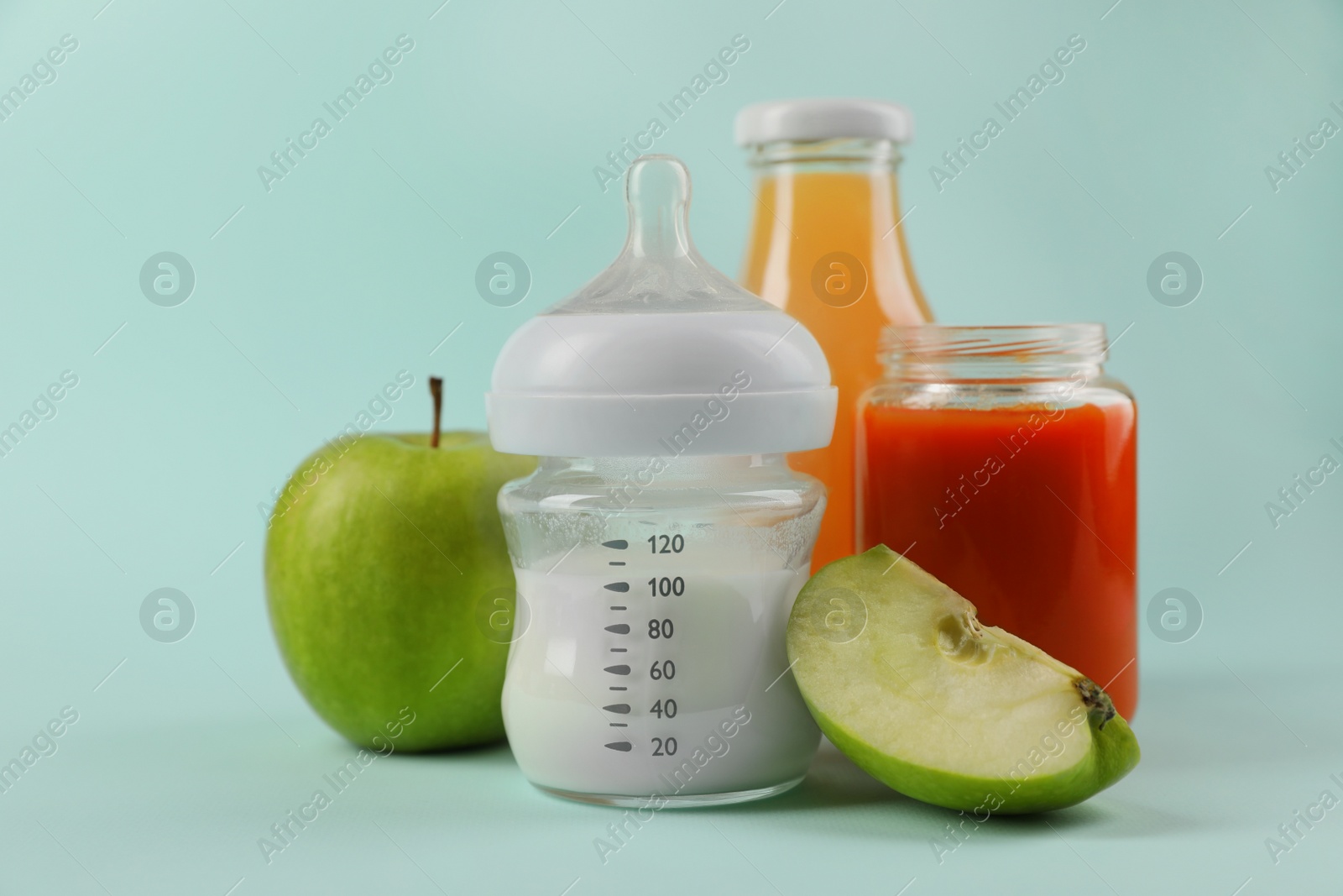 Photo of Healthy baby food, apple, milk and juice on light blue background