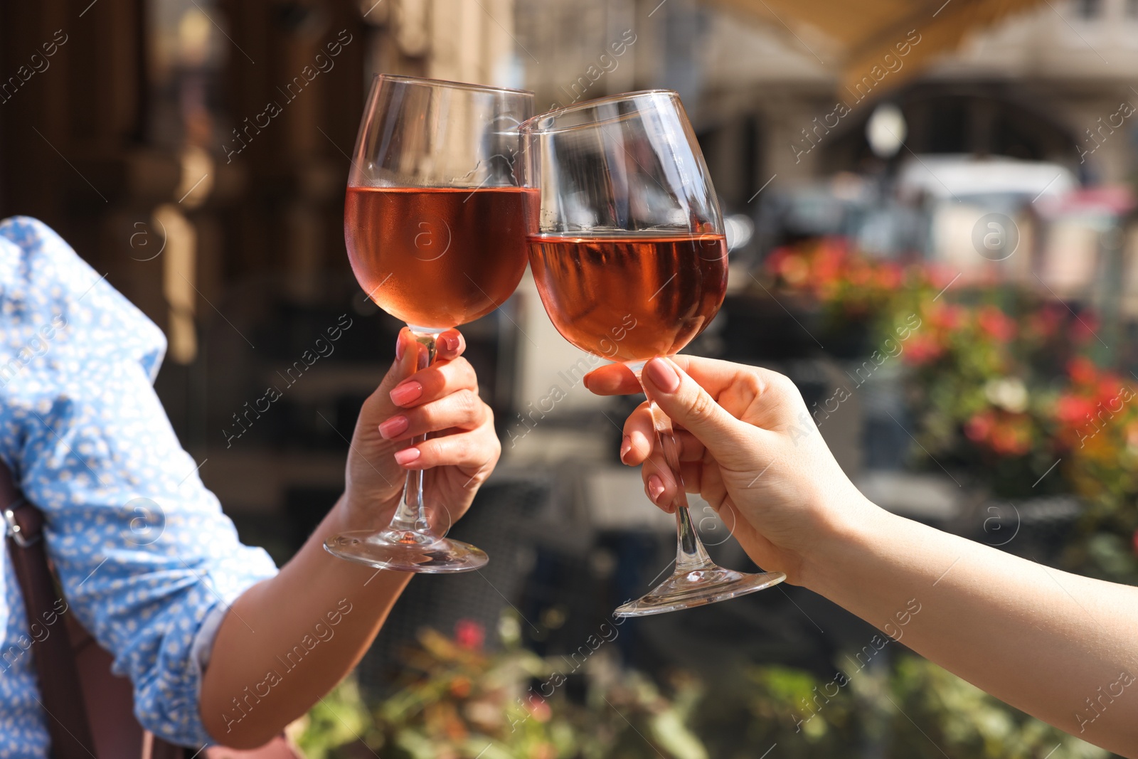 Photo of Women clinking glasses with rose wine in outdoor cafe, closeup