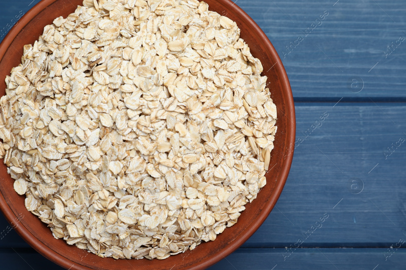 Photo of Bowl of oatmeal on blue wooden table, top view