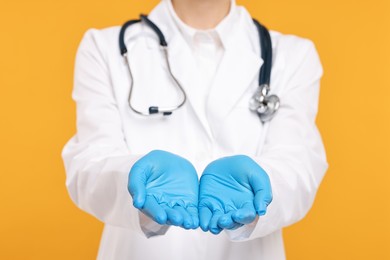 Doctor with stethoscope holding something on orange background, closeup