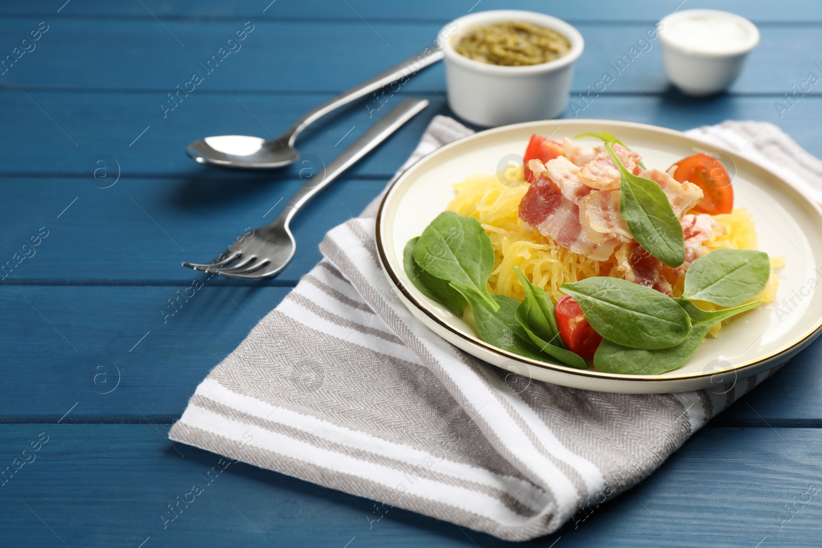 Photo of Tasty spaghetti squash with bacon and basil served on blue wooden table, space for text