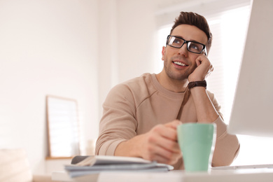 Photo of Young man with cup of drink relaxing at table in office during break