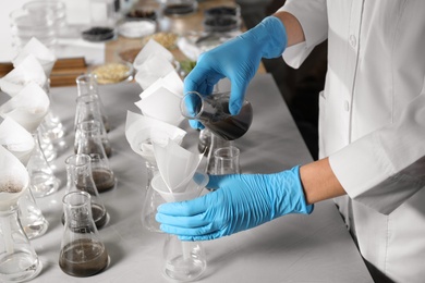 Scientist filtering soil samples at table, closeup. Laboratory analysis
