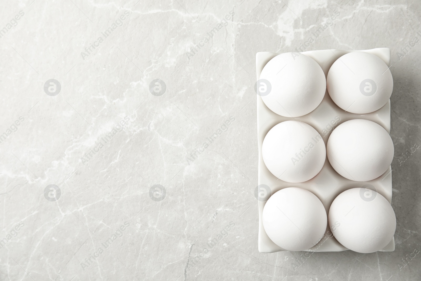 Photo of Raw chicken eggs in ceramic holder on light background, top view. Space for text