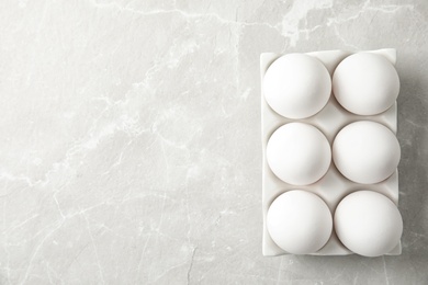 Raw chicken eggs in ceramic holder on light background, top view. Space for text