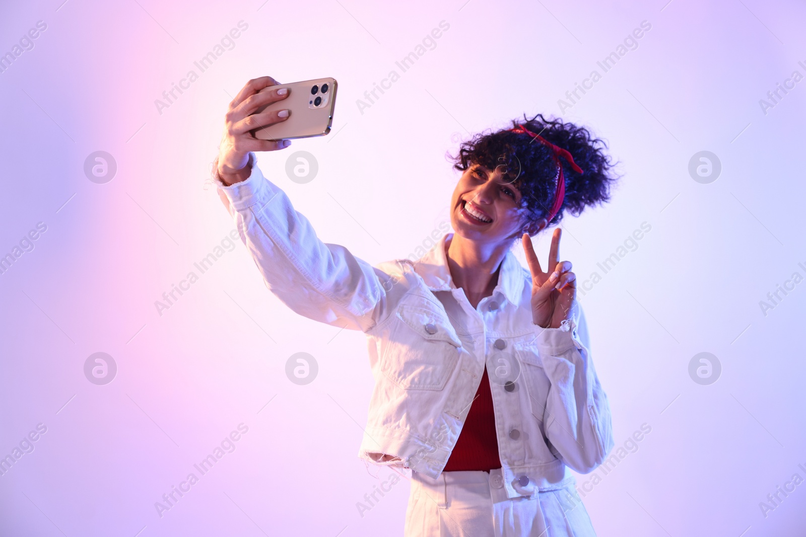 Photo of Beautiful young woman taking selfie on color background in neon lights